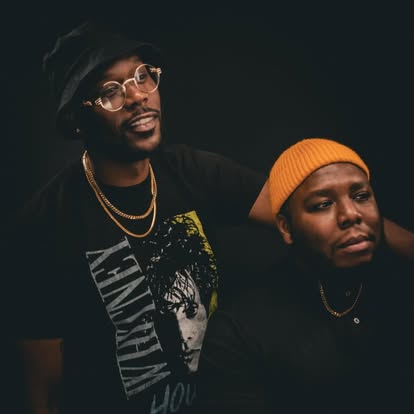 The hosts in a candid studio portrait with black hat and yellow beanie